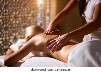 Side shot og massage process in modern wellness center, back of charming girl lying on massage table, having aroma therapy massage with essential oil, indoor shot