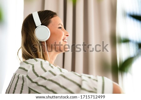 side shot with a woman with headsets listening music or comunication with someone, inside the house next to the bright window and houseplants