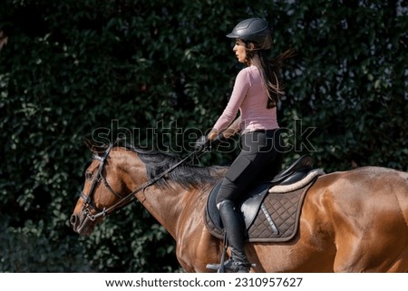 Side shot of a woman riding a horse with bushes in the background