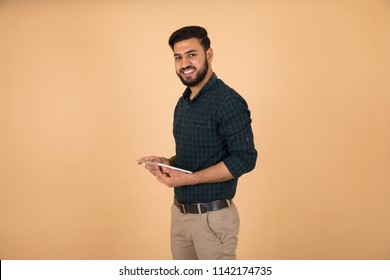 Side shot of young man holding the tablet look directly at the camera smiling on orange background. - Powered by Shutterstock