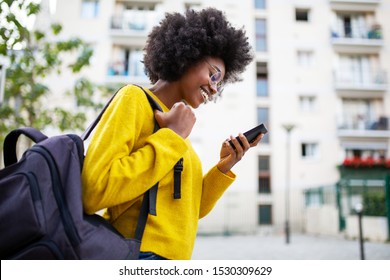 Side of smiling african woman walking in city with bag and phone