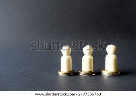 Side studio view of resource distribution, showing three natural wood peg dolls standing on three separate, unequal stacks of coins, against a dark background.