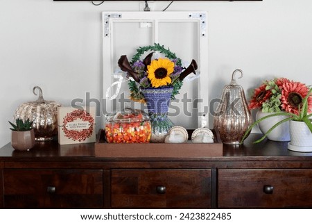 A side table in a kitchen that is full of autumn decorations, candycorn, and a bouquet of flowers.