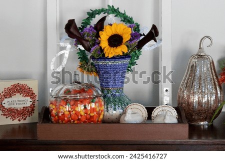 A side table in a kitchen that is full of autumn decorations, candycorn, and a bouquet of flowers.