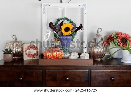 A side table in a kitchen that is full of autumn decorations, candycorn, and a bouquet of flowers.