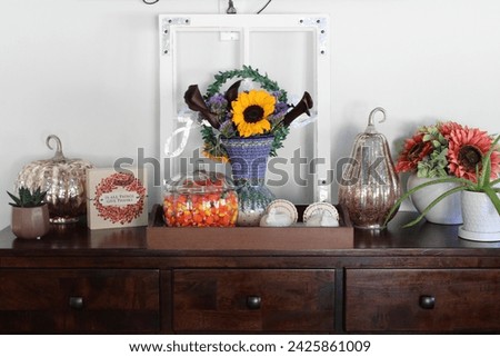 A side table in a kitchen that is full of autumn decorations, candycorn, and a bouquet of flowers.