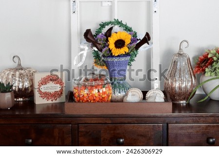 A side table in a kitchen that is full of autumn decorations, candycorn, and a bouquet of flowers.