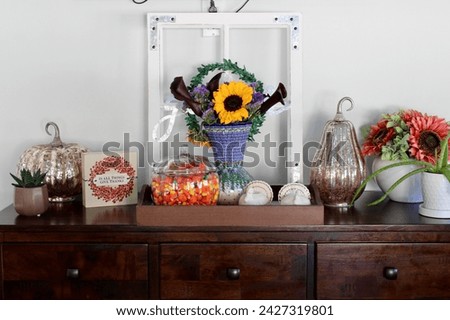 A side table in a kitchen that is full of autumn decorations, candycorn, and a bouquet of flowers.