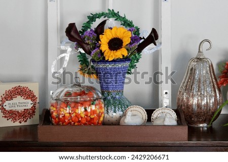 A side table in a kitchen that is full of autumn decorations, candycorn, and a bouquet of flowers.