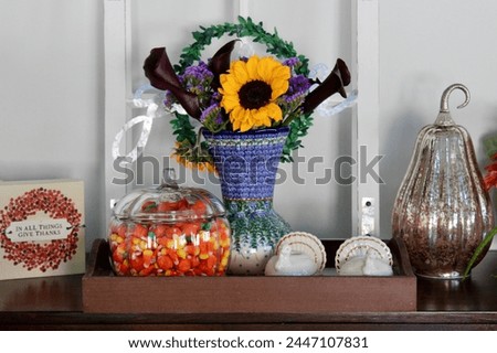 A side table in a kitchen that is full of autumn decorations, candycorn, and a bouquet of flowers.