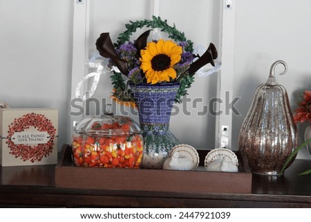 A side table in a kitchen that is full of autumn decorations, candycorn, and a bouquet of flowers.