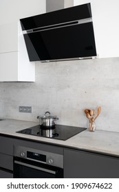 Side and vertical view of saucepan on electric stove under modern cooker hood. Contemporary kitchen with built in appliances, white cupboards, marble countertop and wooden spoons in jar