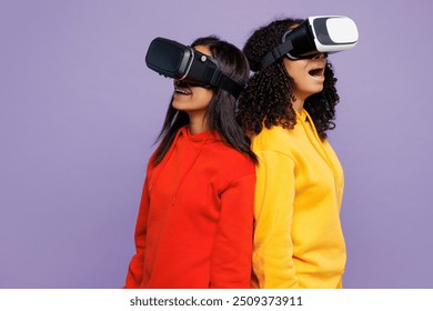 Side vie two young shocked little kid teen girls women they wear red yellow hoodie casual clothes watching in vr headset pc gadget isolated on plain pastel light purple background. Lifestyle concept - Powered by Shutterstock