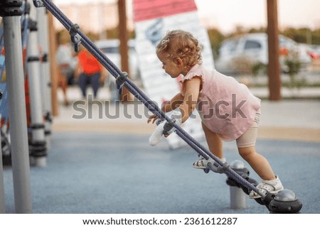 Side view of a 1-3 year old girl climbing a climbing net, rope net or cobwebs on the playground. Toddler with a cast on his arm after playing in the park. White bandage on the arm, plaster on the arm