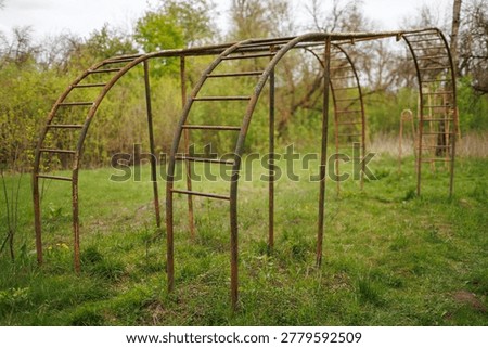 Side view of an abandoned iron monkey bars structure in a rural green area. The metal is covered in rust and peeling green paint.
