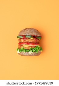 Side View From Above With A Vegan Burger On An Orange Table. Homemade Burger With Soya Patties As A Meat Substitute, Vegan Cheese And Remoulade, And Fresh Vegetables.