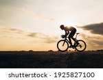 Side view of active sportsman in protective helmet riding bike among nature during sunset. Muscular guy in activewear cycling on paved road.