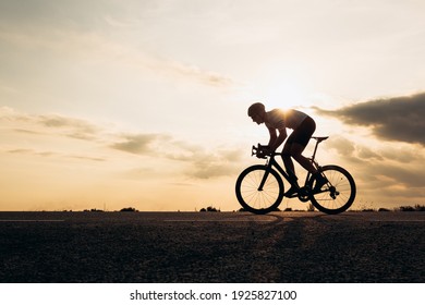 Side view of active sportsman in protective helmet riding bike among nature during sunset. Muscular guy in activewear cycling on paved road. - Shutterstock ID 1925827100