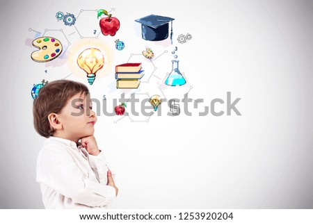 Side view of adorable little boy in white shirt thinking standing near white wall with colorful education sketch. Mock up