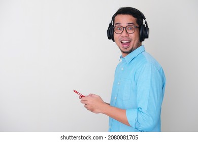 Side View Of Adult Asian Man Wearing Headset And Holding Mobile Phone Showing Excited Expression