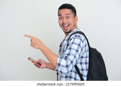Side View Of Adult Asian Man Wearing Backpack And Holding Handphone With Excited Expression