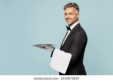 Side view adult barista male waiter butler man wear shirt black suit bow tie elegant uniform hold in hand metal tray plate work at cafe isolated on plain blue background. Restaurant employee concept - Powered by Shutterstock