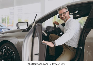 Side view adult cheerful fun man customer male buyer client wear shirt sit in car open door choose auto want to buy new automobile in showroom vehicle salon dealership store motor show. Sales concept - Powered by Shutterstock