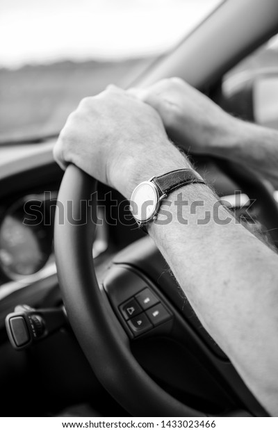 Side view of adult male hands holding firmly\
the steering wheel driving to destination vehicle addapted for\
right-hand traffic - black and white\
image