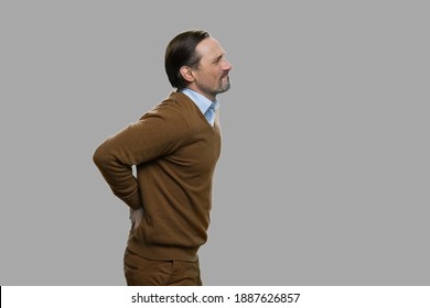 Side view adult man suffering from backache. Unhappy mature man suffering from backache while standing against gray background.