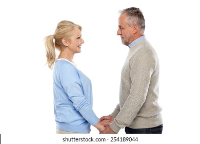 Side view of affectionate mature couple standing together holding hands and looking at each others eyes against  white background 