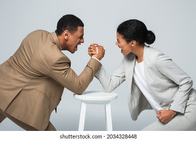 side view of african american businesswoman and man doing arm wrestling on white chair isolated on grey