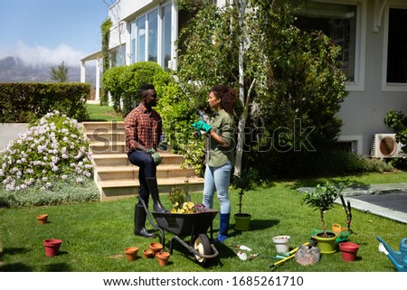 Side view of an African American couple in the garden, standing by a wheelbarrow and talking. Social distancing and self isolation in quarantine lockdown for Coronavirus Covid19