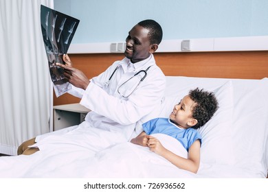 Side View Of African American Doctor And Little Patient Looking At Xray Picture Together In Hospital