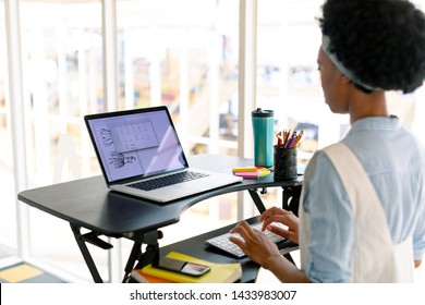 Side view of African american female graphic designer working on laptop at desk in office - Powered by Shutterstock