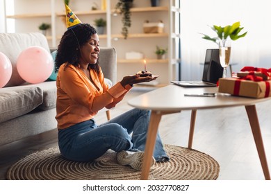 Side View Of African American Female Holding Birthday Cake Sitting At Laptop Celebrating B-Day And Having Virtual Online Party Via Video Call At Home. Remote Holiday Celebration