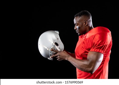 Side View Of An African American Male American Football Player Wearing A Team Uniform And Pads, Holding His Helmet Before Putting It On