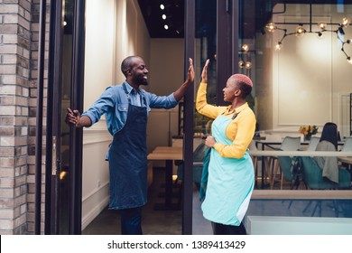 Side view of African American man and woman smiling and doing high five to each other while opening cafe for customers - Powered by Shutterstock