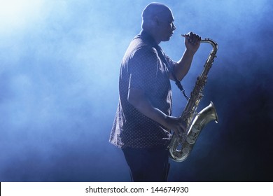 Side view of an African American man playing saxophone against smoky background