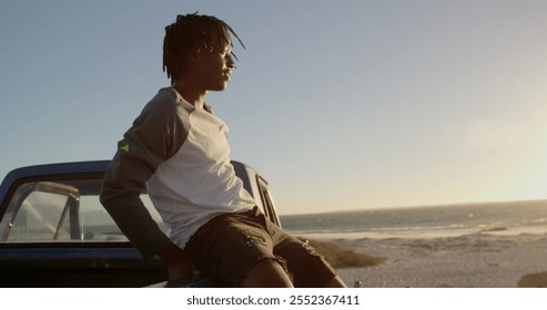 Side view of African american man sitting on trunk of pickup truck at beach. He is looking at sea 4k - Powered by Shutterstock