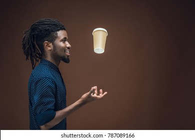 Side View Of African American Man Tossing Up Coffee In Paper Cup Isolated On Brown