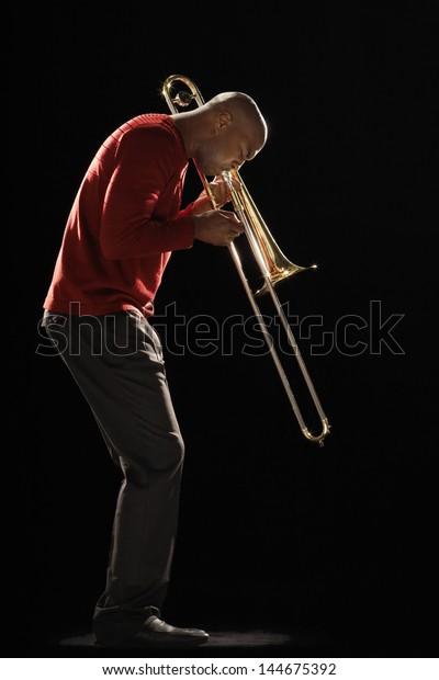 Side view of an African American man playing\
the trombone against black\
background