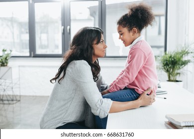 side view of african american mother talking with her daughter indoors