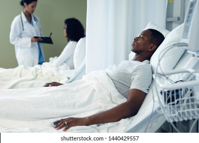 Side View Of African American Patient Sleeping In Bed While Mixed Race Female Discussing With Mixed Race Patient At Hospital