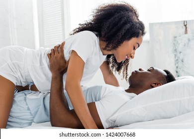 side view of african american woman kissing boyfriend, lying on bed