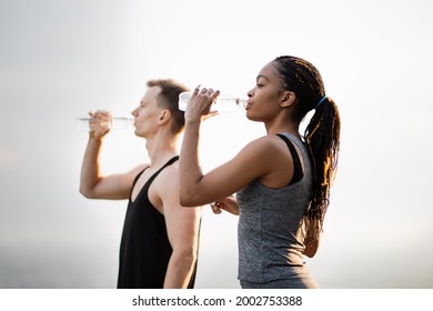 Side view of african american woman and caucasian man refreshing with cold water after active outdoors workout. Concept of people,healthy lifestyles and recreation. - Powered by Shutterstock