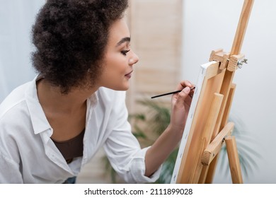 Side View Of African American Woman Painting On Canvas In Living Room