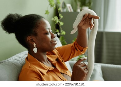 Side view of African American woman with white rat snake in hands sitting in front of camera and cuddling her pet creeping over arm - Powered by Shutterstock