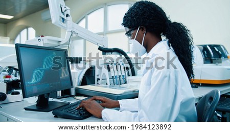 Side view of African American young female medical expert sitting at workplace in lab working typing on computer looking at molecular structure. Scientist using computer in his modern laboratory
