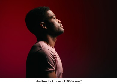 Side view of african handsome young man with neutral calm face expression standing in t-shirt on dark red background - Powered by Shutterstock