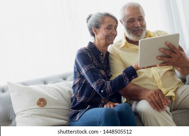 Side view of African-American couple sitting on a couch while using digital tablet. Authentic Senior Retired Life Concept - Powered by Shutterstock